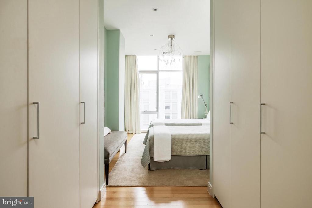 Bedroom with built-in wardrobes, a bed, bench, chandelier, and large curtained window.