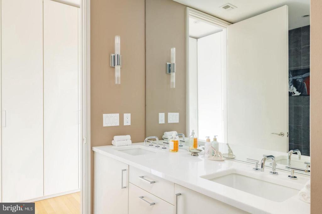 Bathroom with a white double-sink vanity, large mirror, and open door to a dark-tiled shower.