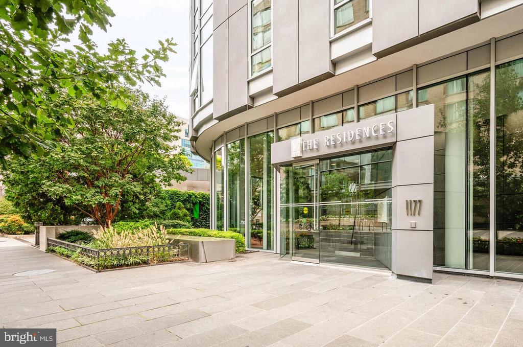 Modern residential building entrance marked 1177, with glass doors and leafy landscaping.
