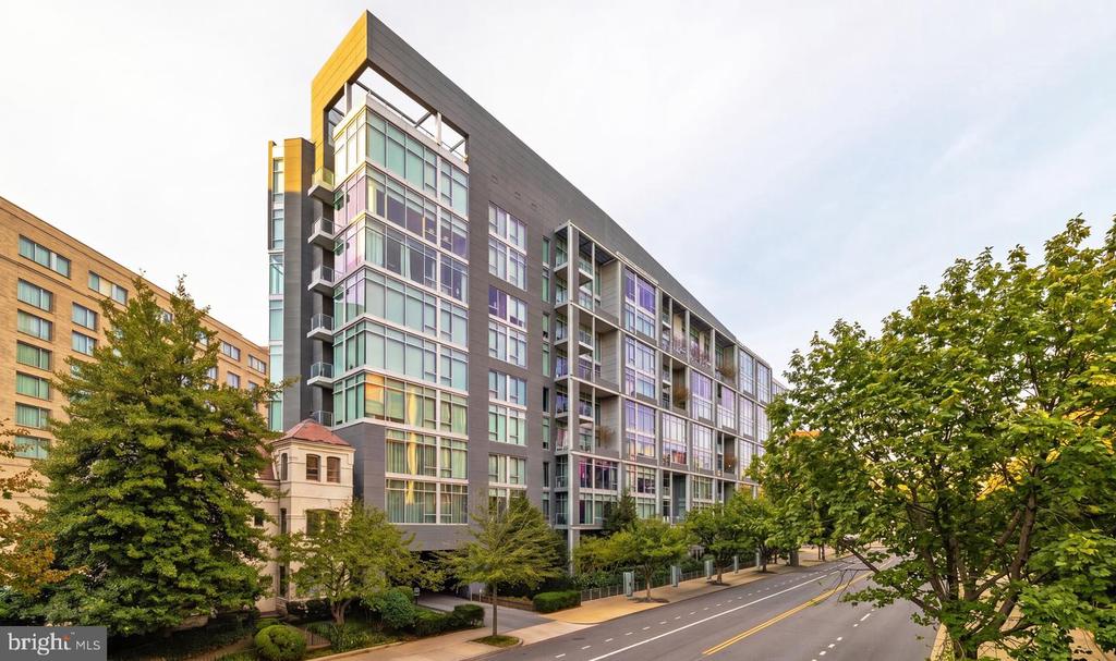 Modern residential building with glass balconies and a gold-accented corner along a tree-lined street.