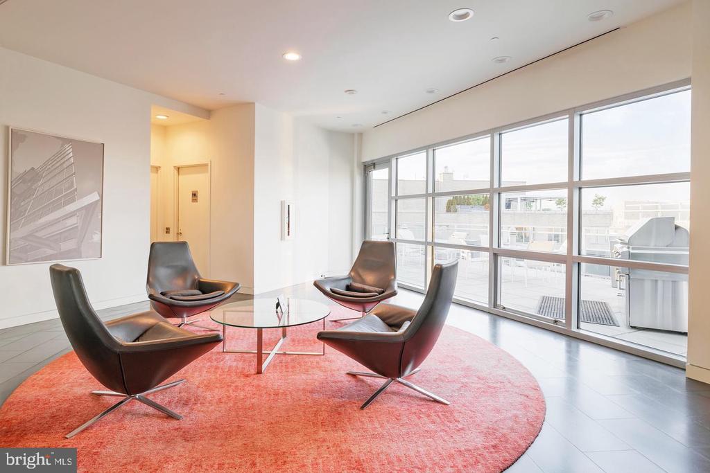 Furnished sitting area with modern leather chairs, a coral rug, and floor-to-ceiling windows opening onto a terrace.