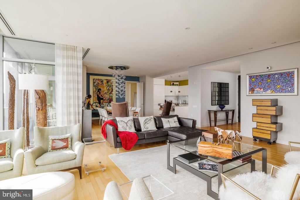 Living room with a dark sectional, cream armchairs, floor-to-ceiling windows, and colorful artwork.