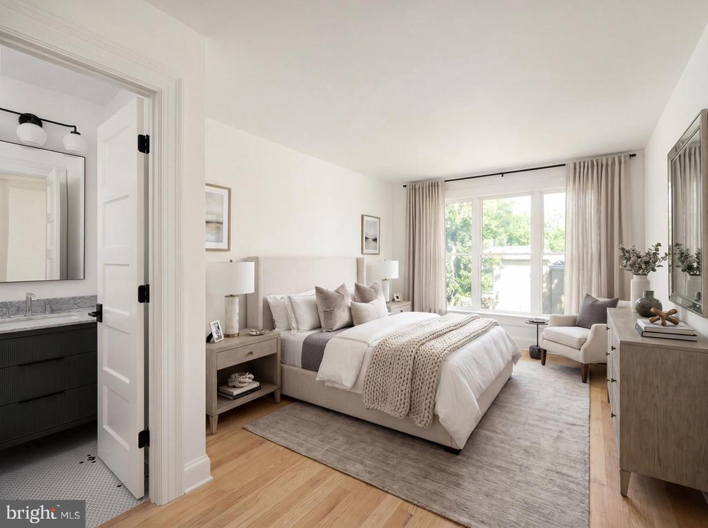 Staged bedroom with a king-size bed, large curtained windows, hardwood floors, and an adjoining bathroom.