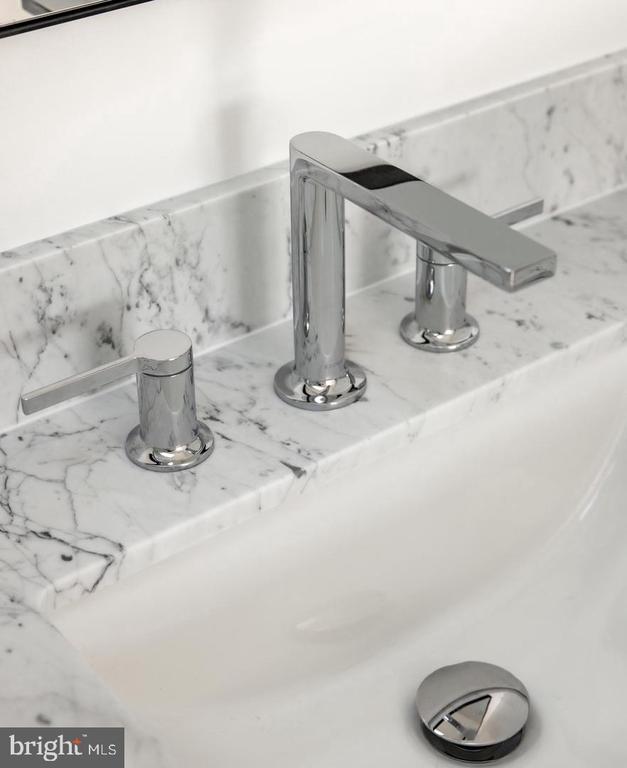 Bathroom faucet with chrome handles on a white veined marble countertop.