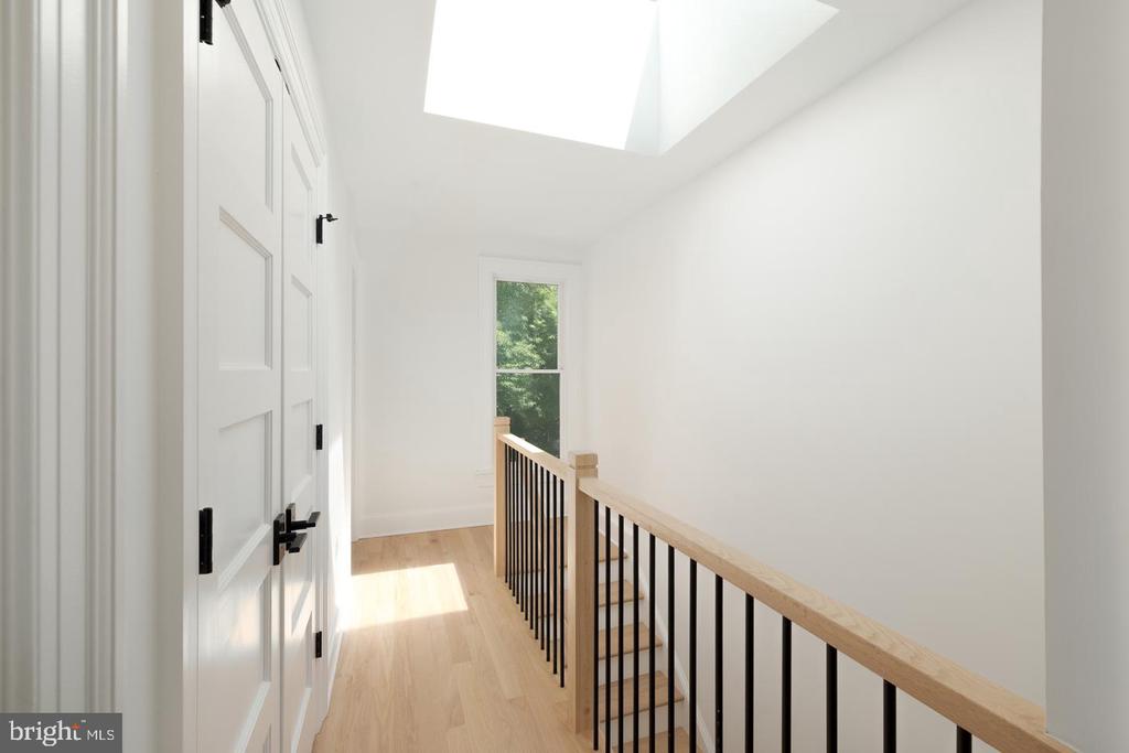 Upper-floor hallway with a skylight, light wood flooring, and black stair railing