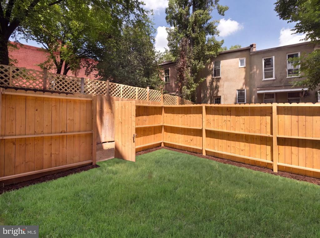 Fenced backyard with a green lawn, wooden privacy fence, and open gate.