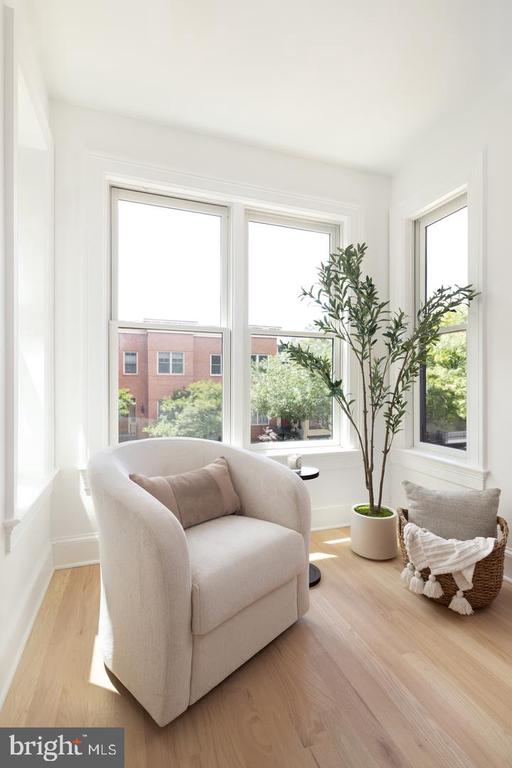 Bright sitting area with a curved cream armchair, potted tree, and large windows overlooking trees.