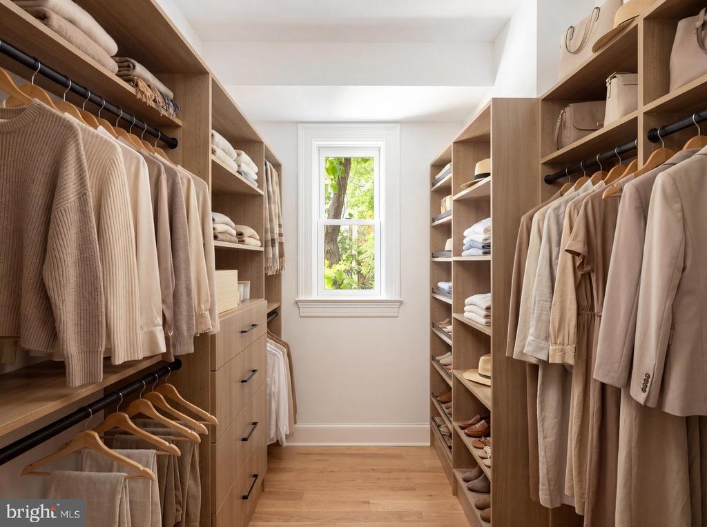 Walk-in closet with built-in wooden wardrobes, neutral clothing, organized shelves, and a window overlooking greenery.