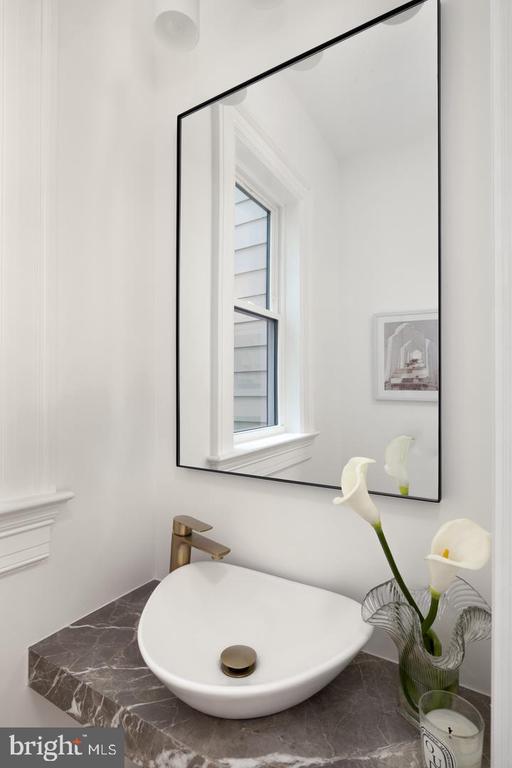 Bathroom vessel sink with brass faucet, dark marble counter, black-framed mirror, and calla lilies.