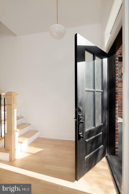 Entryway with an open black glass-paneled door, pale hardwood floors, and a light wood staircase.