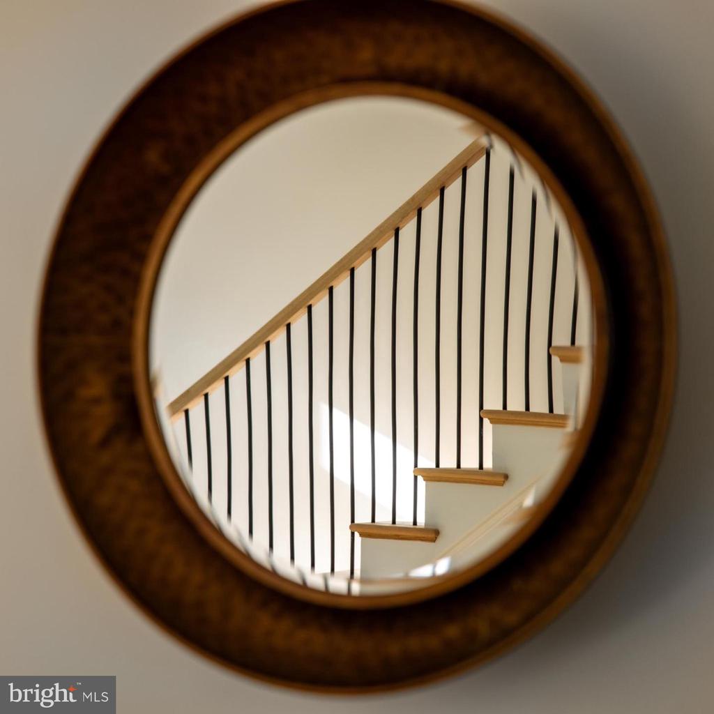 Staircase with wood treads and black balusters reflected in a round wall mirror.