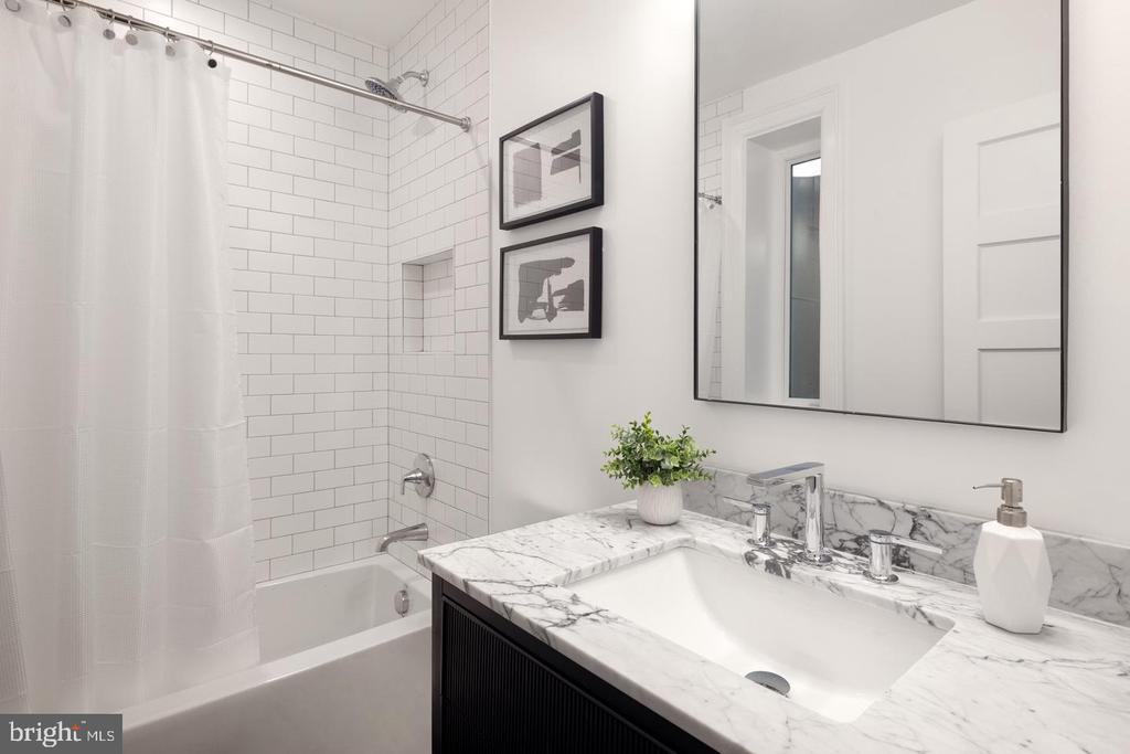 Bathroom with a marble vanity, subway-tile tub surround, and large mirror.