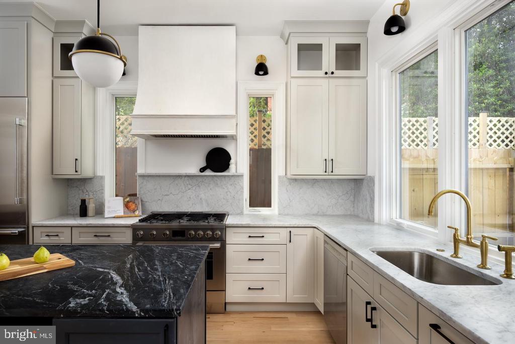 Kitchen with white cabinets, marble counters, a black island, and a large window overlooking a fenced yard.