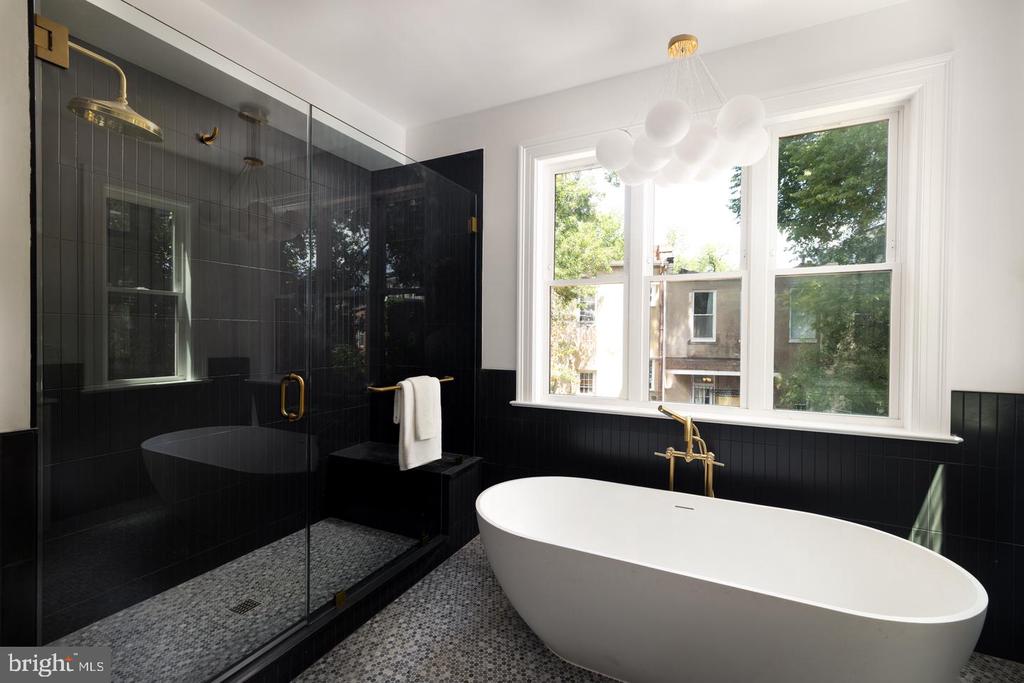 Bathroom with a freestanding soaking tub, black-tiled glass shower, and large windows.