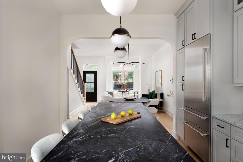 Kitchen with a dark marble island, gray cabinetry, and an open view to the living area and staircase.