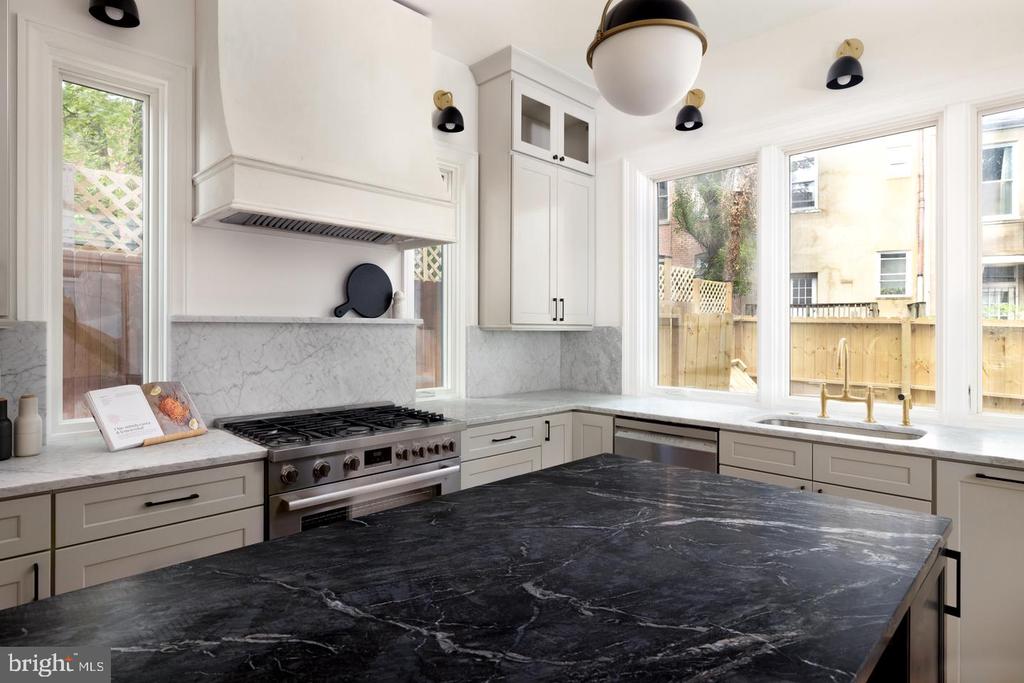 Kitchen with a dramatic black marble island, white cabinetry, and large windows overlooking a fenced yard.
