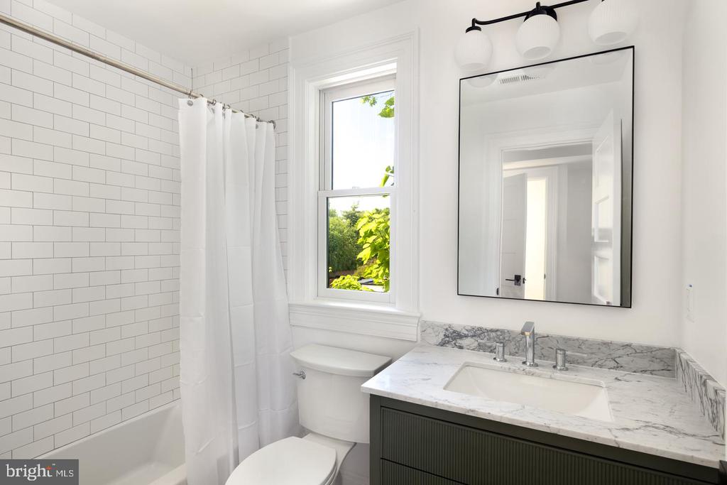 Bathroom with a subway-tile tub, greenery outside the window, and a marble-topped dark vanity.