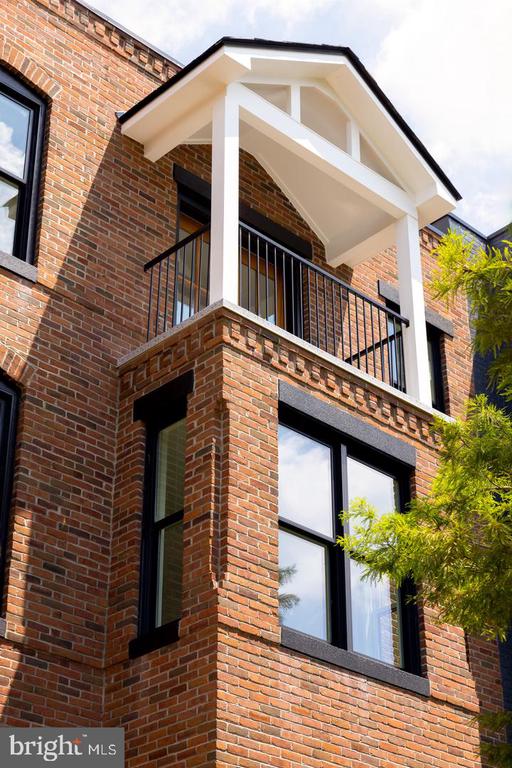 Red-brick townhouse facade with a balcony beneath a white gabled canopy.