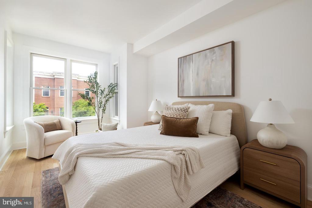 Staged bedroom with a white quilted bed, window-side armchair, and warm wood nightstands.