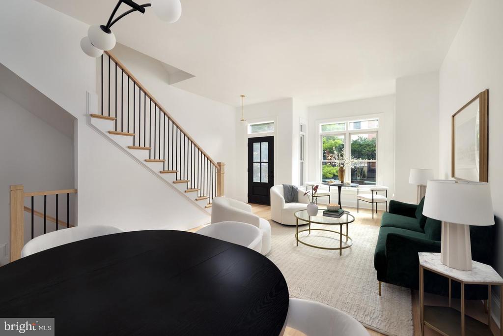 Furnished living and dining area with a staircase, green sofa, and large garden-facing windows.