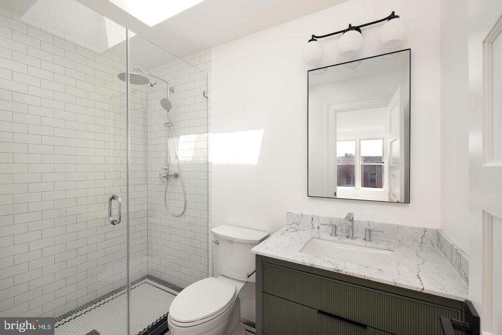 Bathroom with glass-enclosed subway-tile shower and marble vanity with dark green cabinetry.