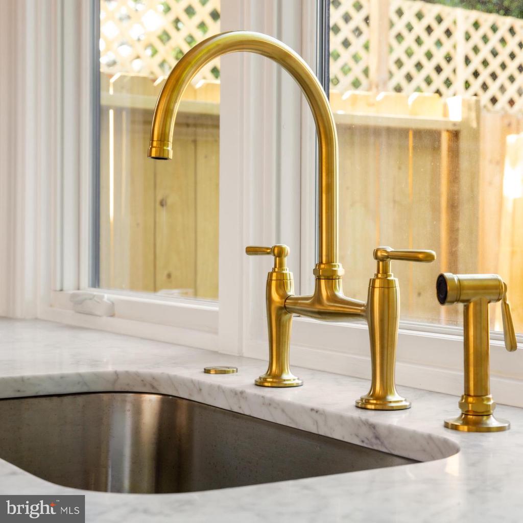 Gold kitchen faucet and side sprayer above a dark sink in a white marble countertop.