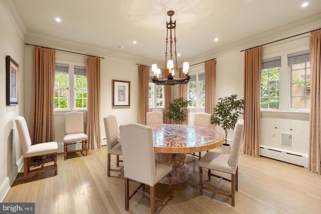 Dining room with a round inlaid table, tall curtained windows, and a chandelier.