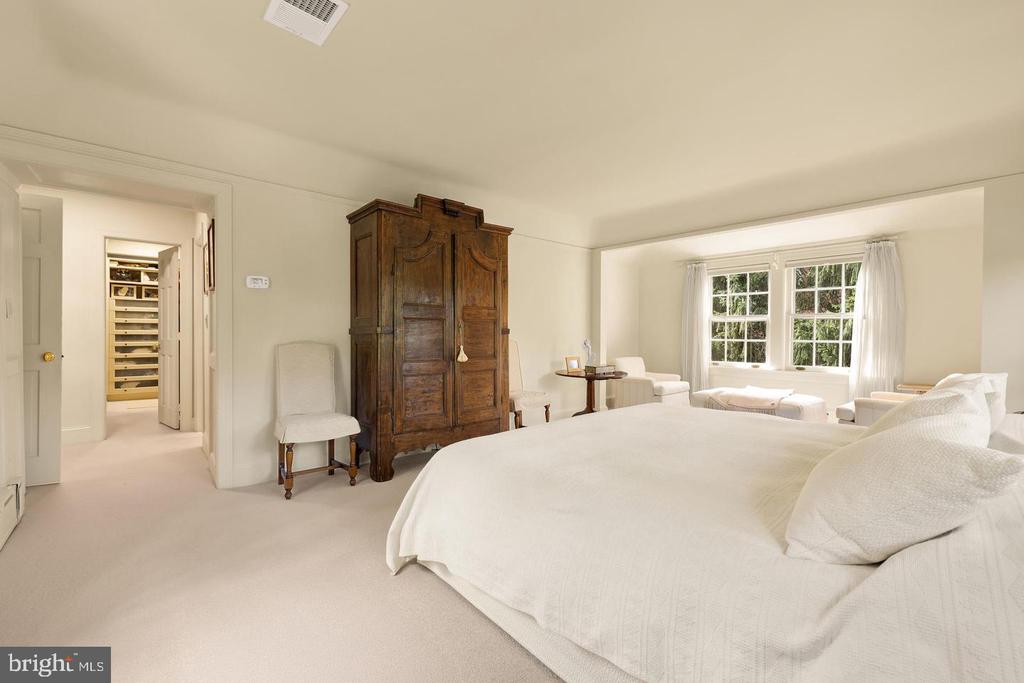 Bedroom with a large white bed, ornate wooden armoire, and window-side sitting area.