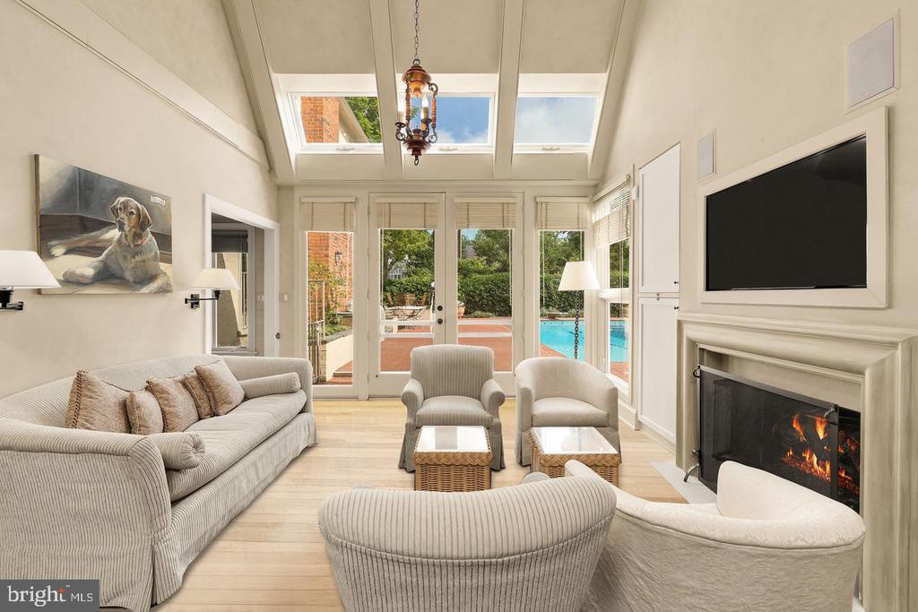 Living room with a vaulted skylit ceiling, fireplace, and doors opening to a patio and pool.