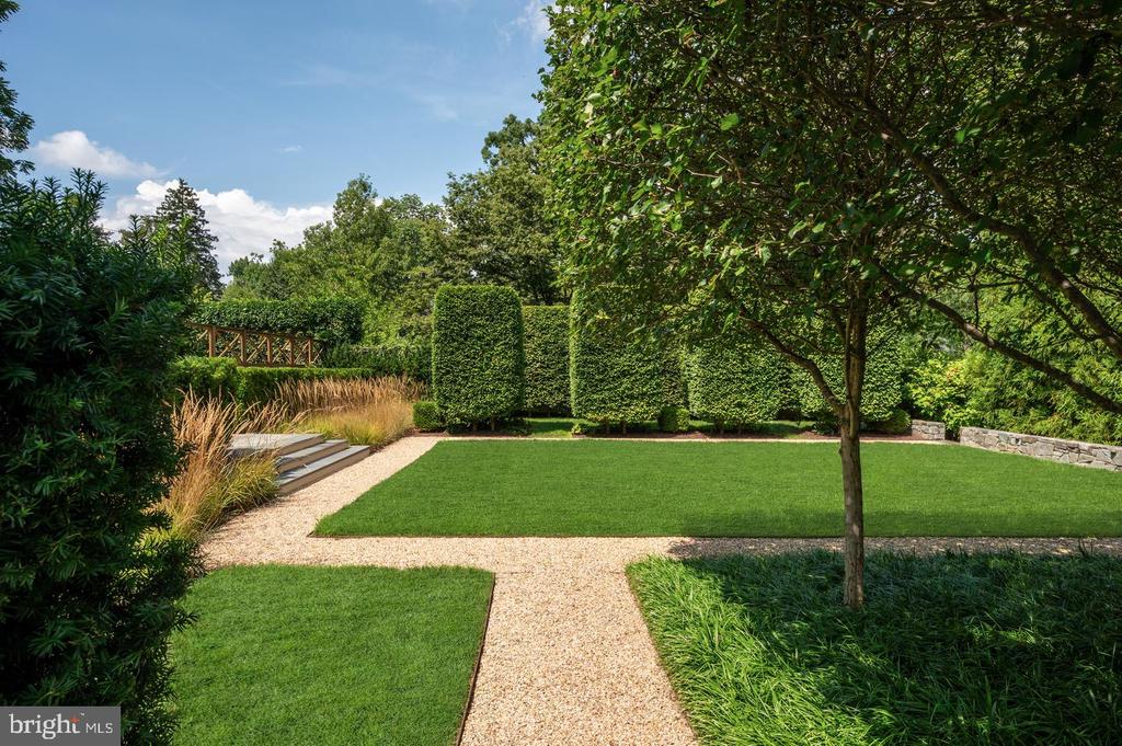 Landscaped garden with clipped lawns, gravel paths, sculpted hedges, and a mature shade tree.