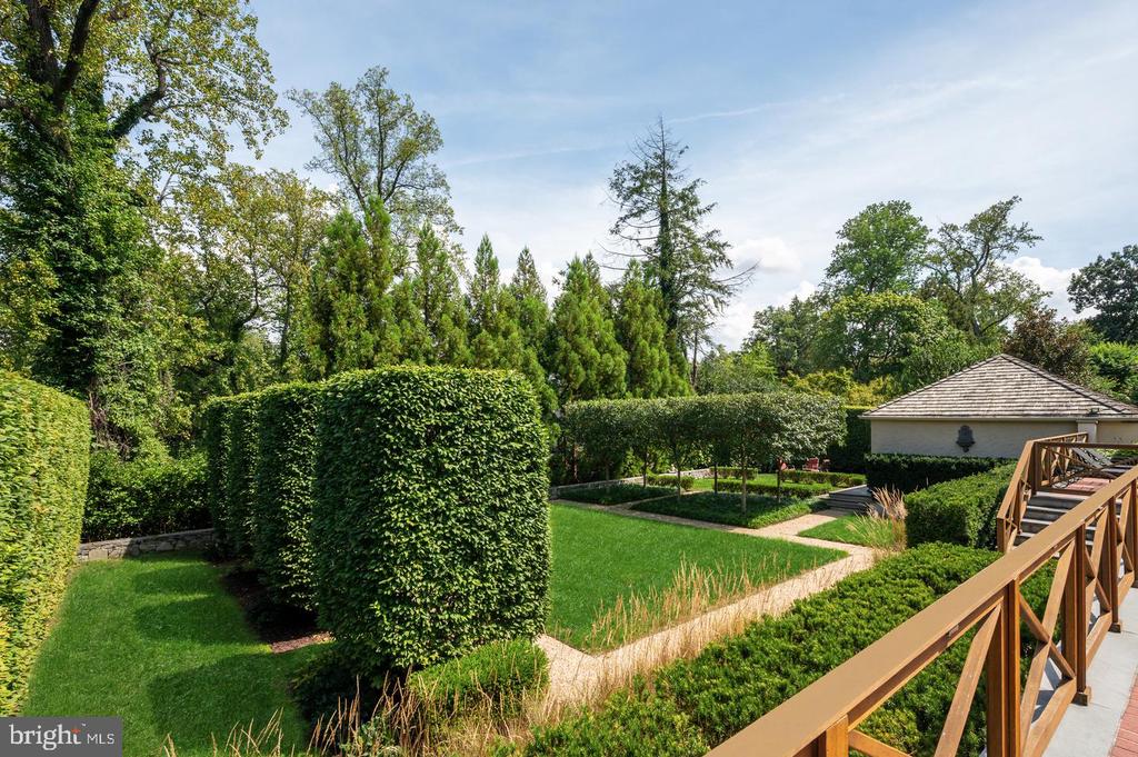 Landscaped backyard with clipped hedges, winding stone paths, and a wooden-railed deck.