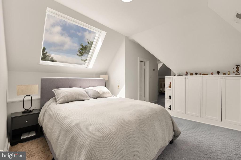 Attic bedroom with a large bed, sloped ceiling, skylight, and built-in white cabinets.