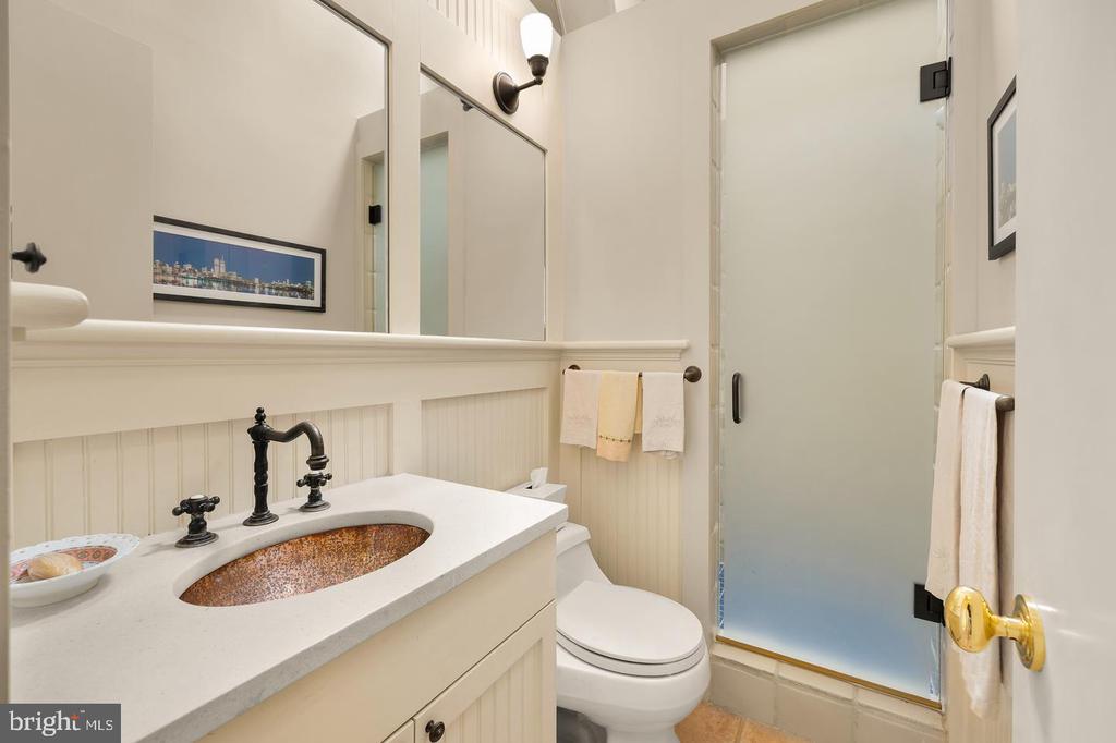 Bathroom with a copper-colored sink, black faucet, beadboard paneling, and frosted-glass shower.