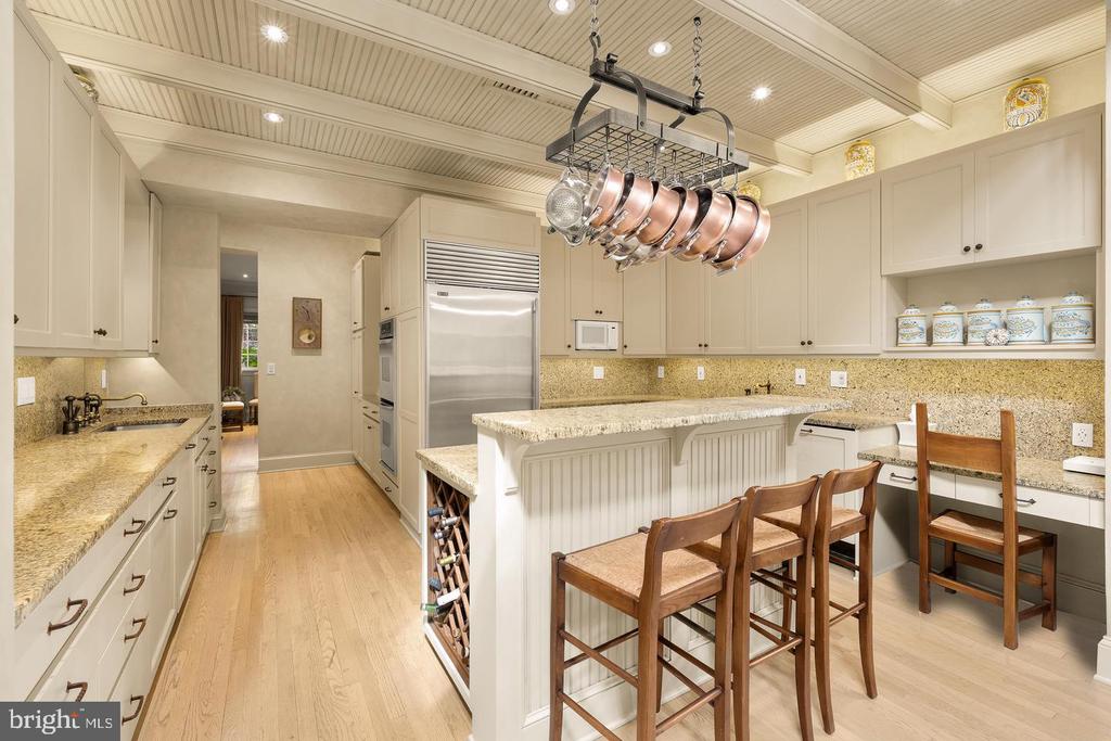 Kitchen with a large island, wooden stools, cream cabinetry, and a ceiling-mounted pot rack.