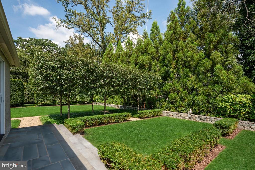 Landscaped backyard with a broad lawn, clipped hedges, mature trees, and a slate patio.
