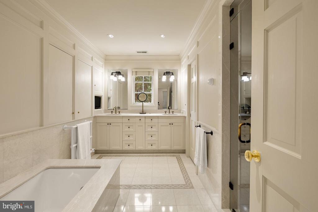 Spacious cream bathroom with a double-sink vanity, foreground bathtub, and glass shower.