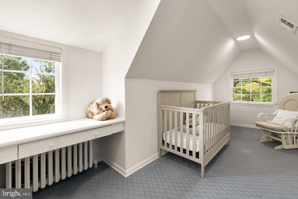 Nursery with a crib, window seat, and rocking chair beneath a vaulted ceiling.