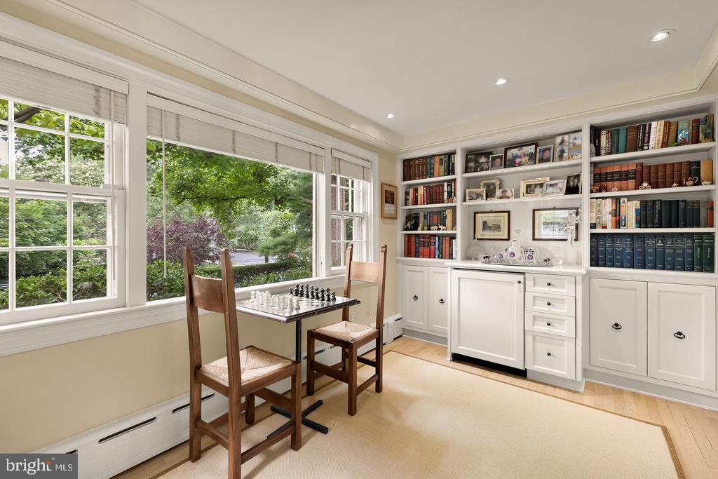 Home office with built-in bookcases, a chess table, and large windows overlooking greenery.