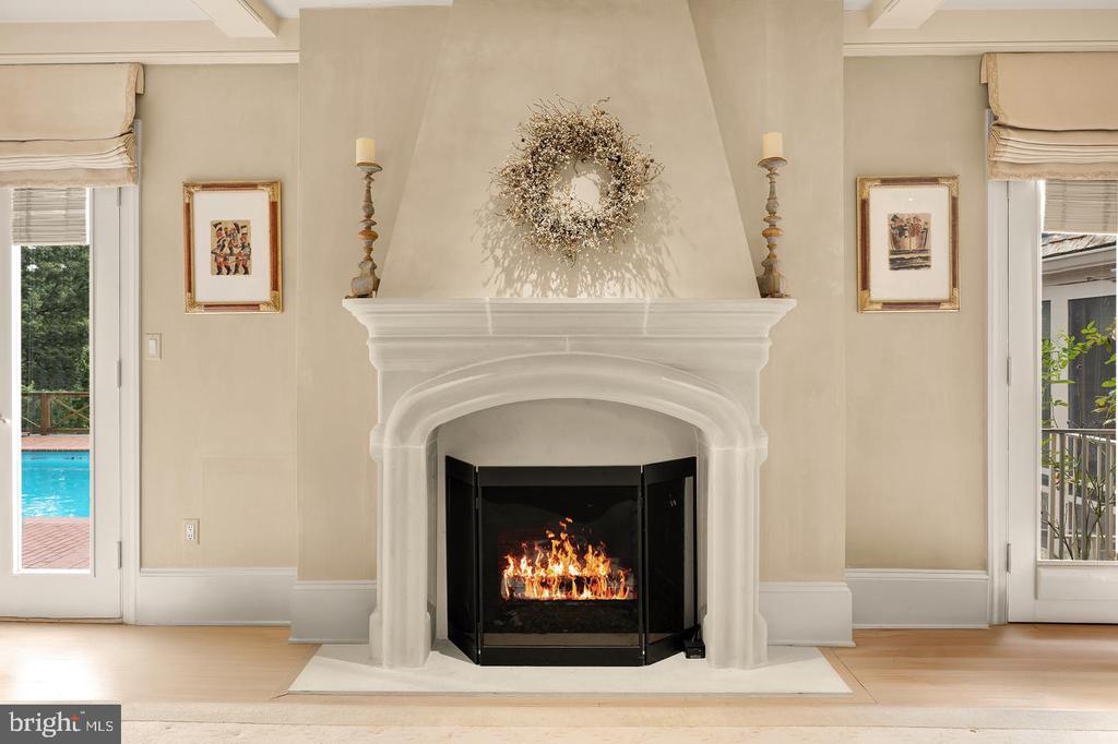 Living room with an arched white fireplace, burning fire, and a swimming pool visible through the doors.