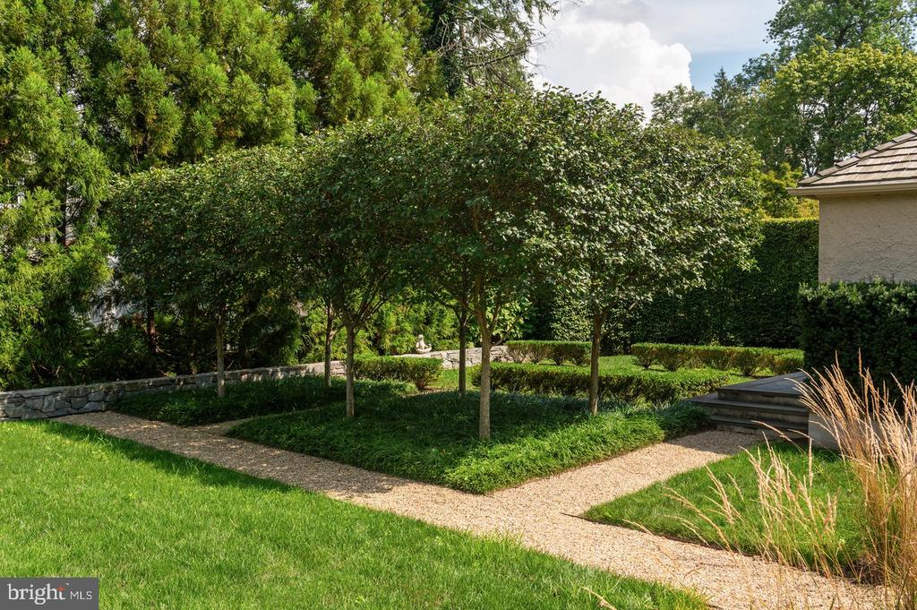 Landscaped garden with a curving gravel path, small trees, clipped hedges, and stone wall.