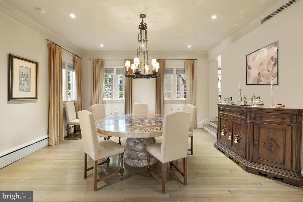 Dining room with a round stone-top table, cream chairs, curtained windows, and a dark wood sideboard.