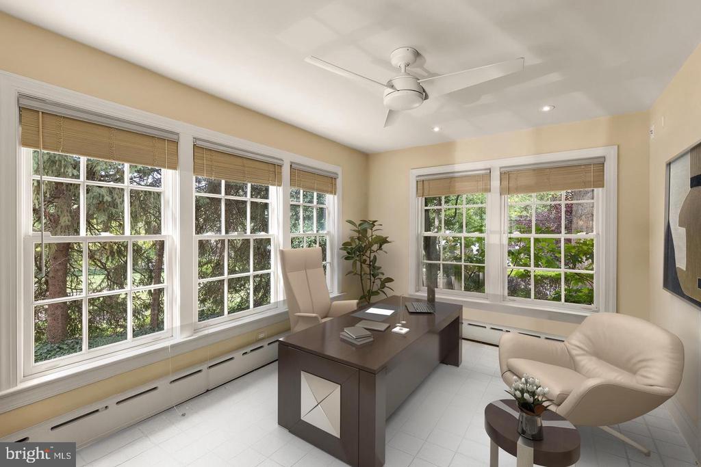 Furnished home office with a dark desk and large windows overlooking greenery.