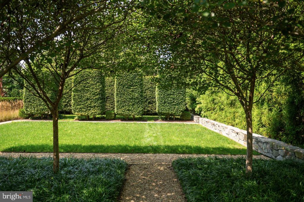 Landscaped garden with a bright lawn, mature trees, clipped hedges, and a stone wall.