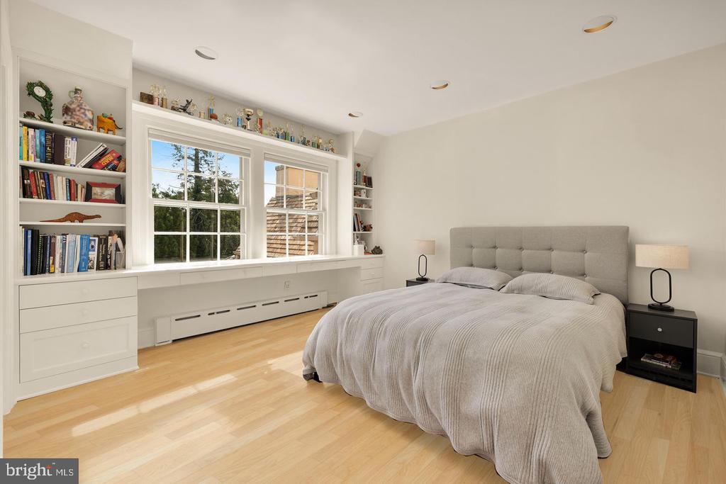 Bedroom with a tufted gray bed and built-in bookshelves surrounding two windows.
