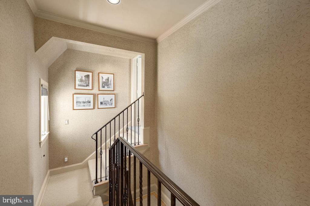 Carpeted staircase with dark iron railings, patterned wallpaper, and framed photographs on the landing.