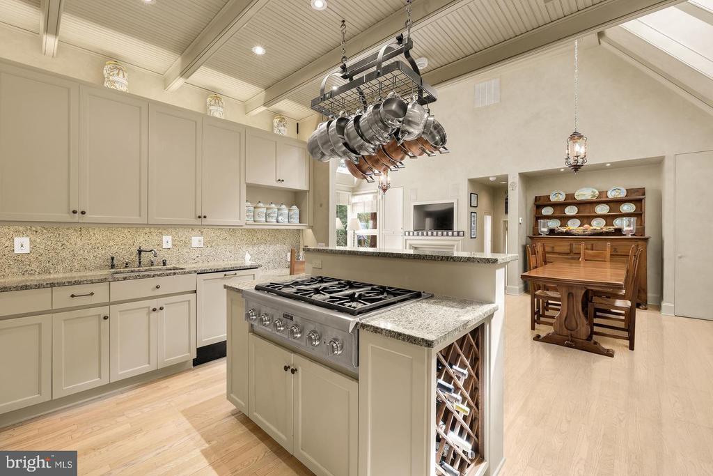Kitchen with a large gas-cooktop island, hanging pot rack, and adjoining dining area.