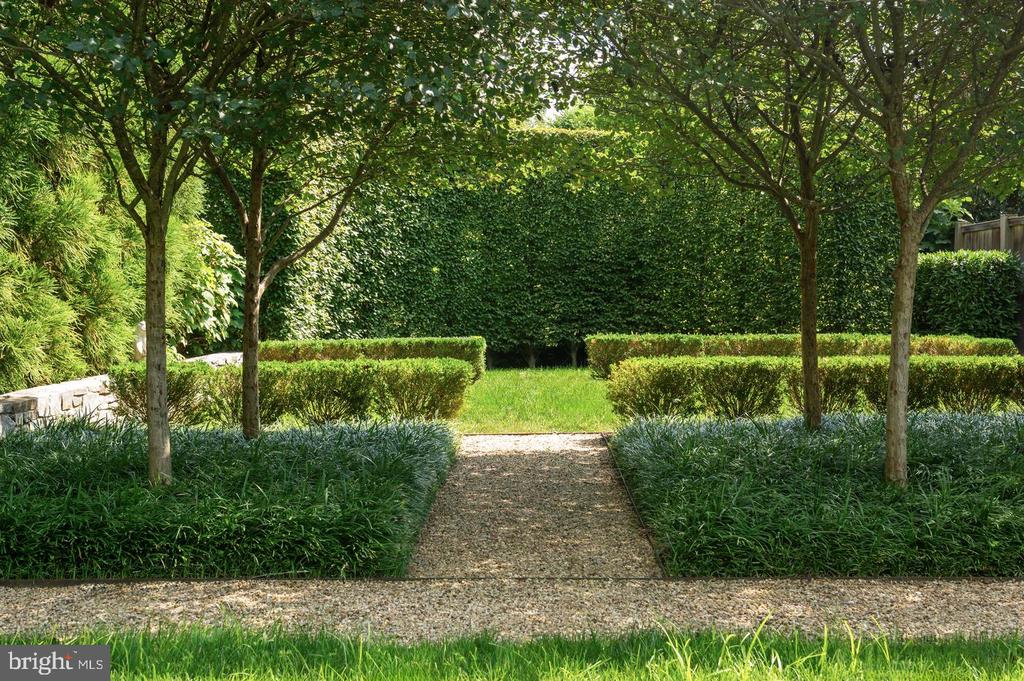 Landscaped garden with a gravel path between clipped hedges and mature trees.