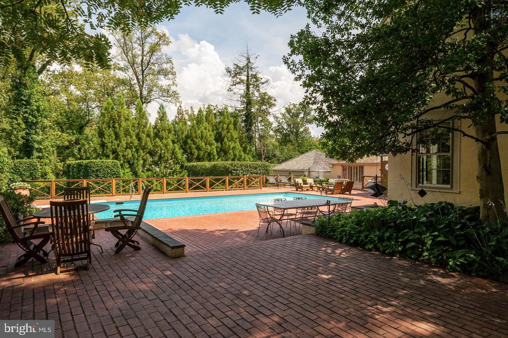 Swimming pool beside a brick patio with outdoor dining furniture and mature trees.