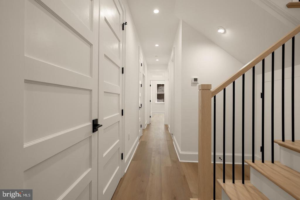 Bright hallway with white paneled doors, light wood floors, and a staircase with black balusters.