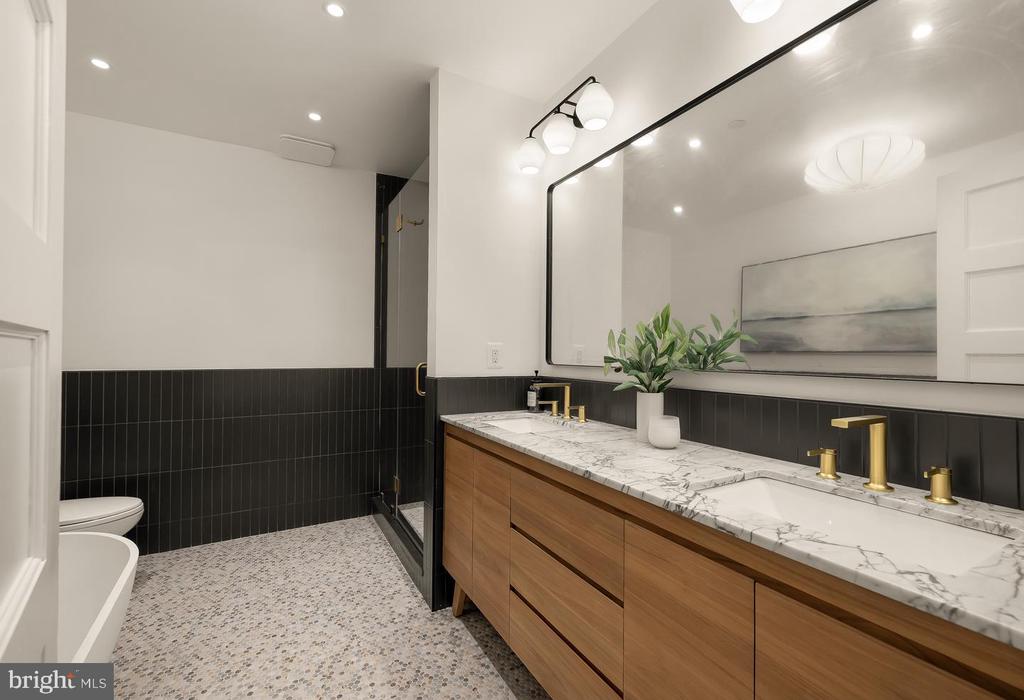 Bathroom with a long wood double vanity, marble countertop, brass faucets, black tile, and glass shower.